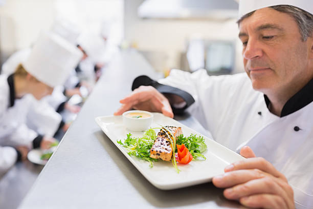 istock Head chef examining dish as other chefs are preparing 459211427