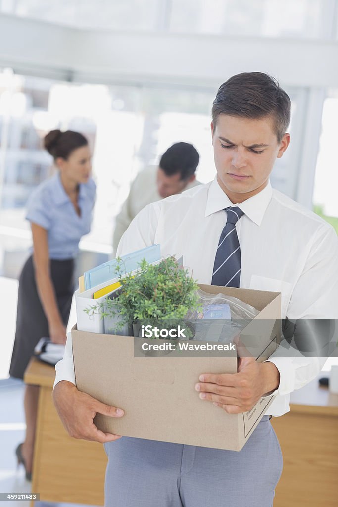 Upset businessman leaving office after being laid off Upset businessman leaving office after being laid off carrying box of his things 20-29 Years Stock Photo