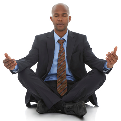 An African-American businessman sitting meditating against a white background