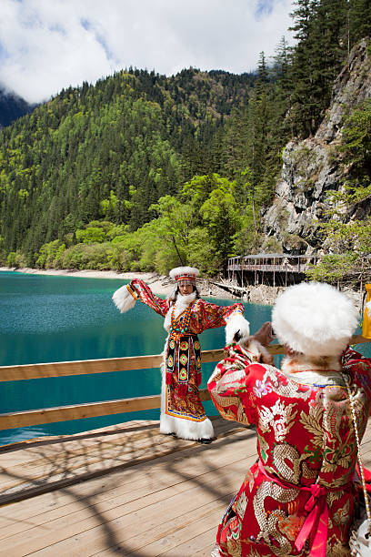 Jiuzhaigou, China - May 14, 2011: Han Chinese tourists wearing traditional Tibetan clothes taking photographies in front of the Panda Lake at Jiuzhaigou. The lake takes is name from the Giant Pandas which are said to come and drink its water. It is at an elevation of 2590 m