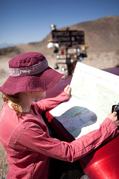 Young woman looking at map in Death Valley National Park Death Valley National Park, California - March 20, 2009:A young woman is looking at a map of the Racetrack area of Death Valley. In the background is Teakettle Junction, a sign that is covered with a number of teakettles. teakettle junction stock pictures, royalty-free photos & images