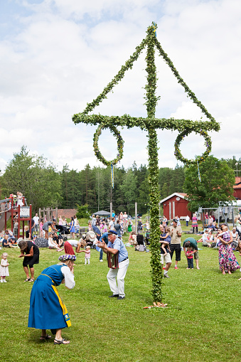 Domarudden, Sweden - June, 24th 2011: People standing around the Midsummer Pole in Sweden. A girl in swedish traditional clothes in foreground.