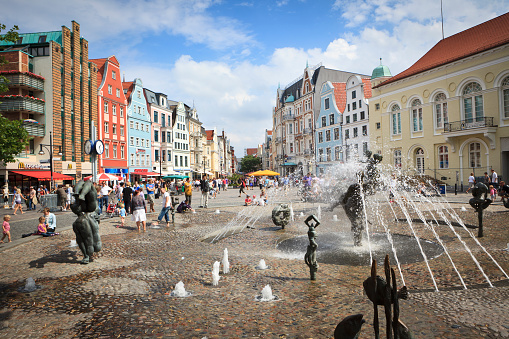 Rostock, Germany - August 6, 2011: University square with Fountain of Zest for Life in the center of the city of Rostock. Children playing in the fountain, their parents observing them. Historic buildings around the square. Rostock lies directly at the Baltic Sea and belonged to the Hanseatic League of cities. It is the largest city in the German state Mecklenburg-Vorpommern.