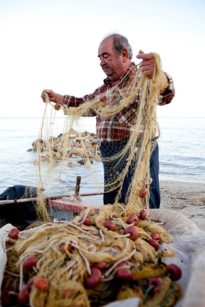 Northern Greece - November 13, 2009: An old Greek fisherman sorting out his nets on the shore along the east coast of Northern Greece, in a small fishing village south of Thessaloniki.