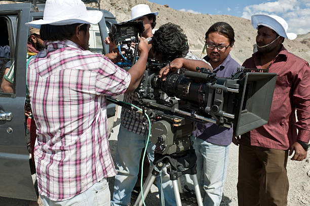 Caucasian Camera Operator Behind Modern Digital Cinema Equipment in Dark Blue Studio Light. Lens and Matte Box Close Up. Cinema and Television Industry Theme.