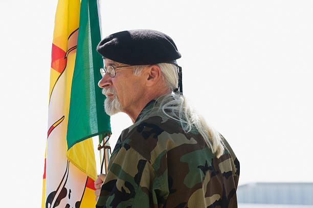 Fosston, USA - August 27, 2011:  On a street corner, against an overcast sky, stands a man wearing a beret and camouflage Army fatigues.  He is holding a Native American Vietnam Veteran flag.  Across the street (out of the photo) where he is looking toward, the Patriot Guard Riders have formed a flag line where a funeral is about to be held for an American soldier who was killed in Afghanistan.