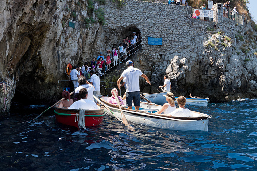 Capri, Italy - August 21, 2011:  Tourists on board of the small boats waiting to enter the in the famous Grotta Azzurra of Capri. The only way to enter in the low and narrow mouth of the Grotta Azzurra is aboard small rowing boats, with a capacity for two or three passengers. The entrance is formed by a small natural opening in the rock,about 2 meters wide and high.
