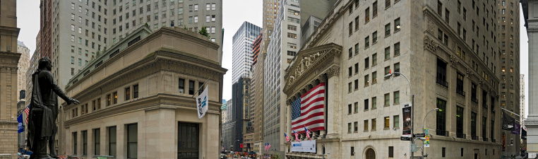 New York, USA - September 9th, 2009: The statue of George Washington on the steps of the Federal Hall National Memorial overlooking the busy intersection of Broad and Wall Streets, home to the iconic portico of the New York Stock Exchange draped in a huge patriotic Stars and Stripes flag. Composite panoramic image created from eight contemporaneous sequential photographs.