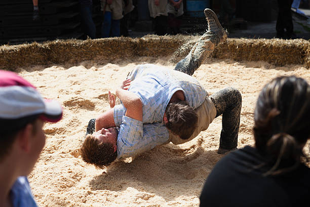 Boltigen, Switzerland - September 3, 2011: Two young men wrestling, surrounded by spectators in Boltigen, Bernese Oberland.  The young men are giving a demonstration in Swiss wrestling, known as Schwingen.  The man on top is just about to beat his opponent as he is in the process of pinning his back to the sawdust covered ground.  The match is taking place at the Farmers Market in Boltigen at the Boltigen train station.Boltigen is located in the Bernese Oberland, Switzerland  in the Simmental where the road from the Jaun Pass reaches the floor of the Simmen valley. It is an agricultural village, and periodically holds a farmer's market on the square next to the train station. The market is frequented primarily by local people.