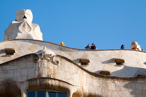 Barcelona, Spain - January, 7th 2013: Some tourists are on roof of Casa MilA  made by Gaudi in Barcelona. At left side is huge expressionistic chimney.