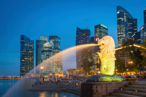 Singapore, Singapore - 14th February 2012: The crowded cityscape of Central Business District skyscrapers overlooking the Merlion fountain on the Marina Bay waterfront at dusk as tourists and locals enjoy the warm evening promenade, Singapore.