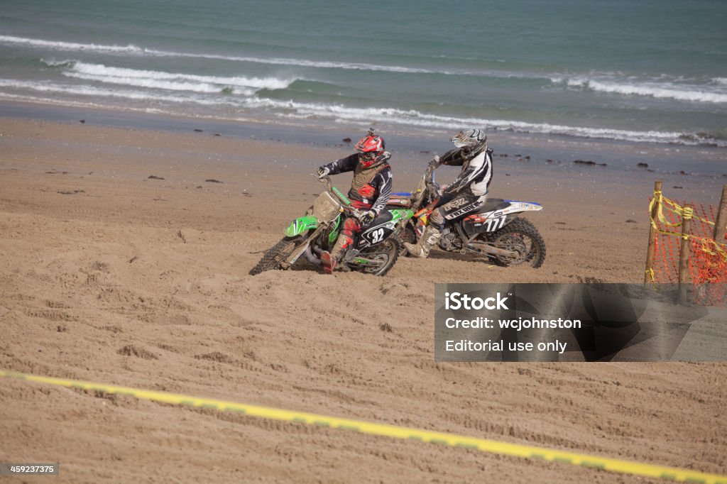 Two motorcycle motocross dirt bikes Weymouth, England - October 20, 2013:  Two motorcycle motocross dirt bike race on the beach at Weymouth Motorcross Race;  yellow tape marks out the track on sand. Sand is thrown into the air by the bikes in the background the sea waves lap on the beach. Beach Stock Photo
