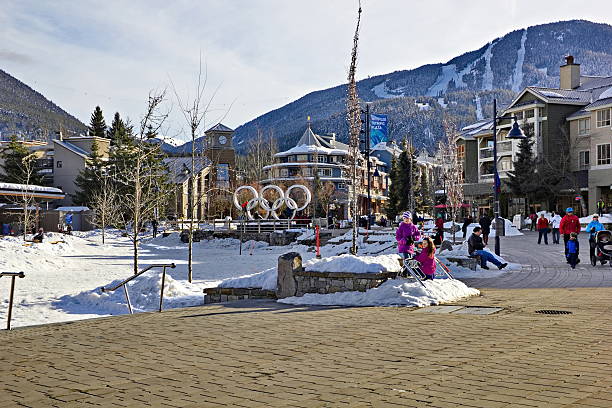 Whistler, Canada - February 10, 2013: Tourists roaming and playing at  Olympic Village, Whistler, British Columbia, on February 10, 2013 with views of Whistler and Blackcomb Mountain behind the village and the peak to peak gondola visible in the distance between the two mountains.