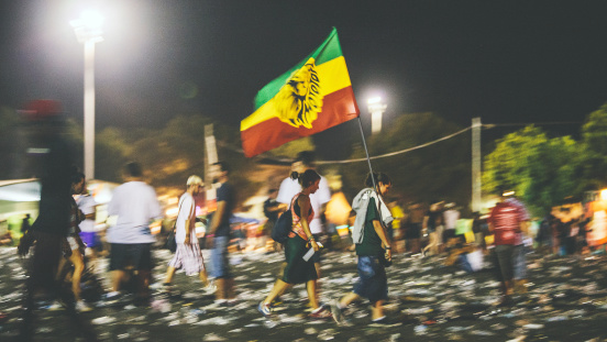 Benicassim, Spain - August 25, 2013: Festival visitors walking with rasta flag over the plastic bottles covered main stage area. Jamaican reggae/dancehall artist Damian Marley just finished his performing. Rototom Sunsplash is biggest reggae festival in Europe and been around for 20 years.