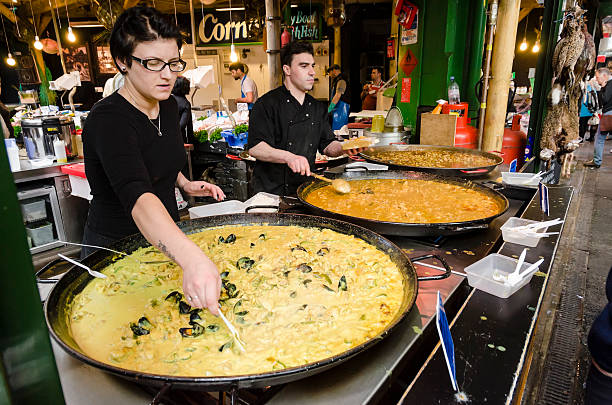 Paella seller at Borough Market London London, UK - October 25, 2013: A female clerk is selling her paella and other ethnic meals at Borough Market in London. She has paella, chicken tandoori and other Asian tastes. Borough market is one of the oldest and largest food markets in central London. borough market stock pictures, royalty-free photos & images
