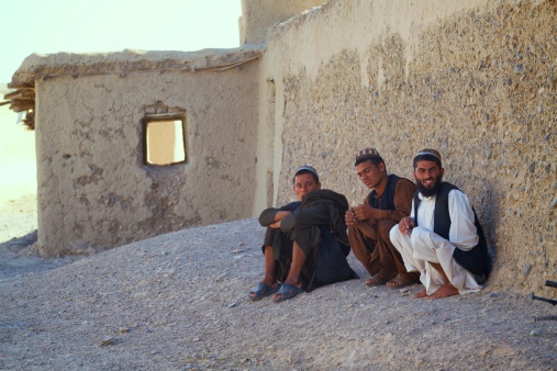 Kandahar, Afghanistan - May 14, 2010: Three Afghan men sit on the side of the road.