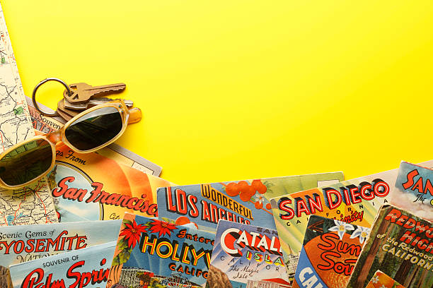 San Diego, California, USA - November 12, 2013: A group of vintage postcards showing various California tourist destinations on top of an old road map of California with sunglasses and car keys.. Shot in a studio setting on a yellow background.