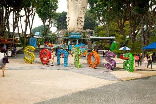 Singapore, Singapore - September, 6th 2012: Scene on square in front of statue of Merlion on Sentosa Island. Asian woman is standing in front of huge letters for photo. In background are walking many people and tourists.