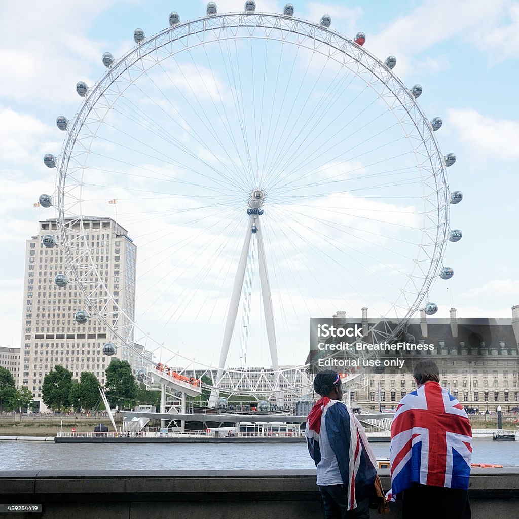 London Eye "London, England - August 1, 2012: Two people with Union Jacks draped over them looking across the river thames at the London Eye during the London 2012 Olympic games." British Culture Stock Photo