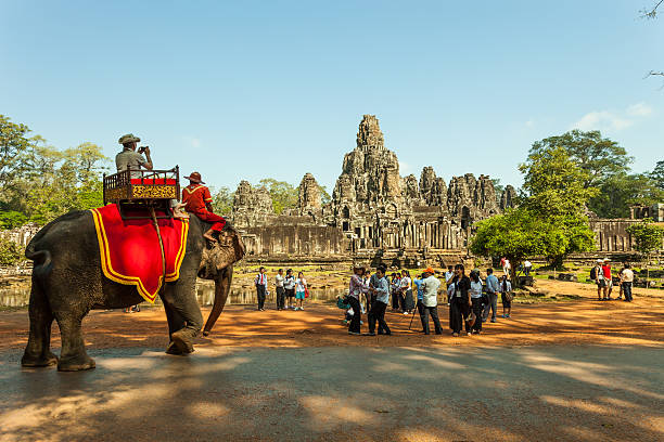 Angkor Vat, Cambodia - September 04, 2019: Towers and Faces at Bayon temple in Angkor Wat. Monk who has umbrella at Bayon Temple with Tourist woman.