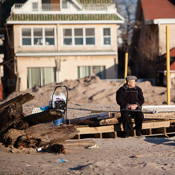 Old man sitting next to ruined homes after Sandy hurrican Brighton Beach, Brooklyn, NY, USA - December 11, 2012: Old man sitting between ruins at Brighton Beach. Parts of a ruined homes still on the Brighton Beach as a consequences of the Sandy hurricane. hurrican stock pictures, royalty-free photos & images