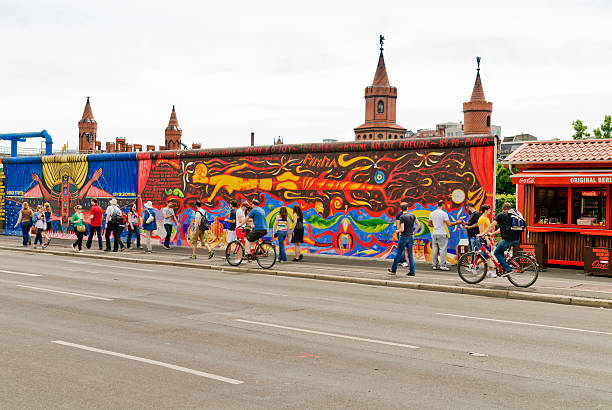 East Side Gallery "Berlin, Germany - May 26, 2012: The Berlin Wall at the Muehlenstrasse. The 3m-high wall separated the city Berlin from 1961 - 1989. Today the remains serve as a memorial and offer artists a space. East Side Gallery the longest wall gallery. The remains of the wall are very popular with tourists. Young people on front of the wall. In the background to see the towers of the Oberbaumbruecke." friedrichshain photos stock pictures, royalty-free photos & images