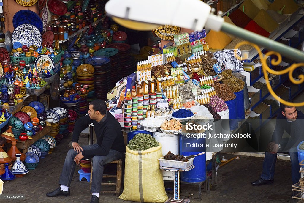 Moroccan merchants "Marrakech, Morocco - December, 15th 2010: Sitting Moroccan merchants inf front of their stores at square of spice market in old medina. At left side are some colorful porcelains. In center are spices, herbs etc.. Aerial shot with tele lens." Adult Stock Photo