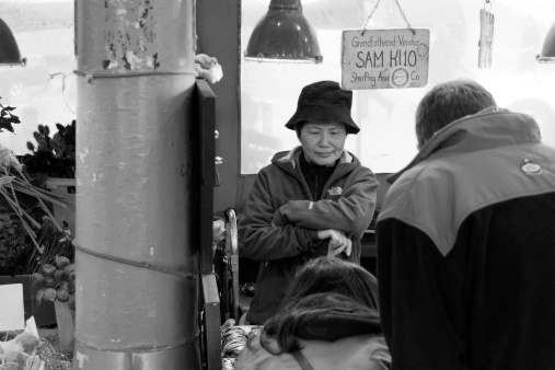 Seattle, WA, USA - October 13, 2012:  An Asian street vendor at Pike Place Market watches and waits as customers select their purchases.