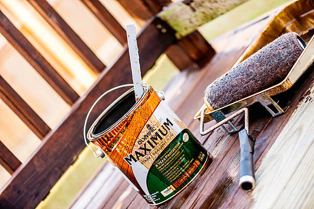 Home Maintenance: Staining a Deck "Suffolk, Virginia, USA - November 11, 2012: A horizontal format shot of a can of Olympic brand Maximum Stain and Sealant All-In-One in shade Canyon Brown, sitting on the floor of an outdoor deck, which is in the process of being painted. Beside the paint can is a paint tray filled with the stain and a paint roller." winterizing stock pictures, royalty-free photos & images