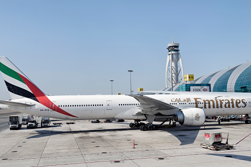 Dubai, United Arab Emirates - January 24, 2013:A Boeing 777 from Emirates Airline is docked at a gate of the new Terminal 3 with the control tower in the background. A service staff is nearby the airplane.