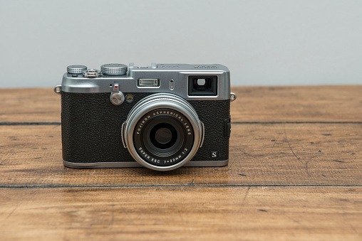 Lancaster, Great Britain - March 27, 2013: Product Shot Fujifilm X100s Digital Camera straight out of the box, photographed on a aged wooden table top against a plain grey wall.