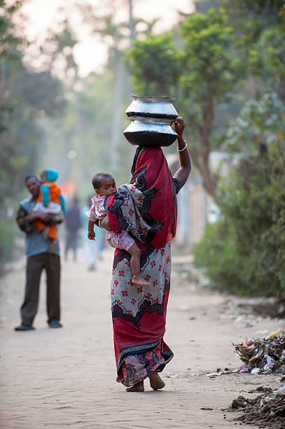 Bengali woman carrying baby and water jar in village "Sylhet, Bangladesh - February 13, 2013: A Bengali woman is carrying her baby and water jars walking in a small village in Srimangal, a small town in Sylhet Division, Bangladesh." sylhet stock pictures, royalty-free photos & images