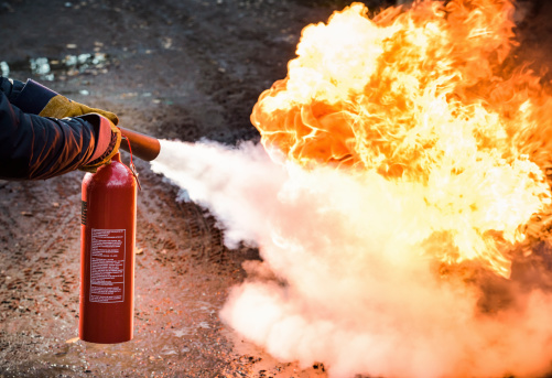 A man using a carbon dioxide fire extinguisher to fight a fire.