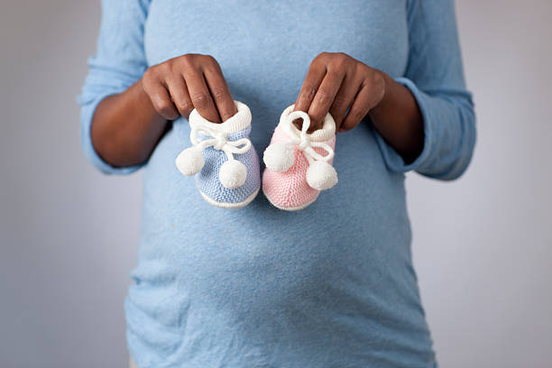Pregnant woman in gender anticipation. Close up image of pregnant woman's belly and hands holding pink and blue tiny baby shoes (front view).