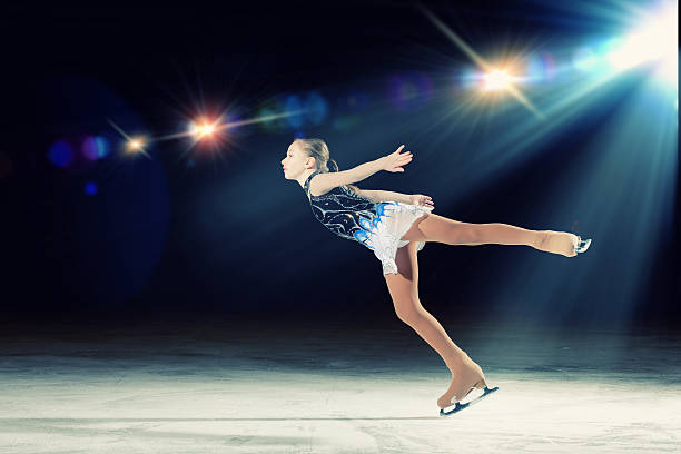 Young girl figure skating with spotlight on her stock photo