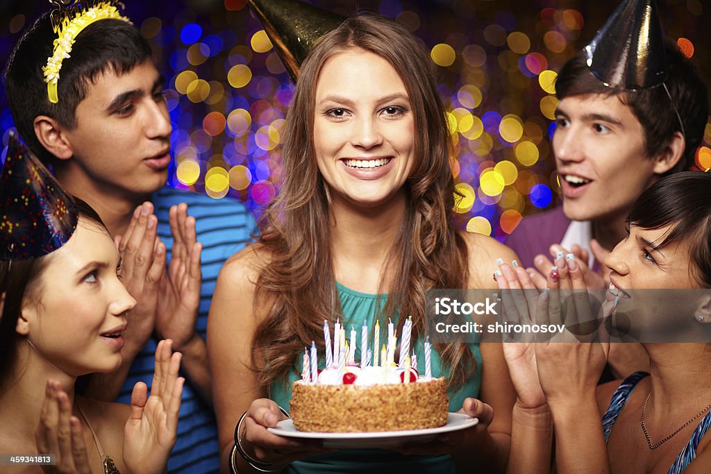 Birthday celebration Portrait of joyful girl holding birthday cake with friends near by at party Birthday Stock Photo