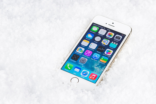 Koszalin, Poland - December 12, 2013: Top view of white iPhone 5S lying on artificial snow. Device display home screen. Close-up shot on iPhone 5S. The iPhone 5S is smartphone with multi touch screen. Device is produced by Apple Computer, Inc.