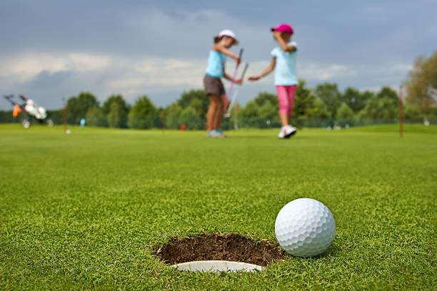 Golf, ball lying on the green next to hole Golf, ball lying on the green next to hole, in the background of the two young golfers golf concentration stock pictures, royalty-free photos & images