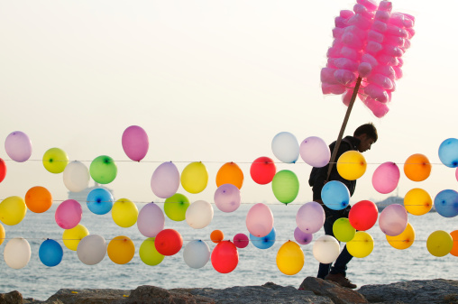 Istanbul, Turkey - May 6, 2010: Vendor selling cotton candy on a stick walks past rows of colorful balloons. The balloons are strung up to be shot down with a bb gun, a game popular with locals on the seaside.