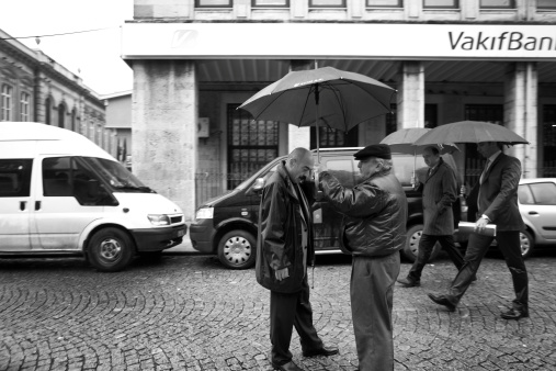 Istanbul, Turkey - November 4, 2009: Two men stand under an umbrella while one of them makes a phone call.  Two other men are passing by in the background carrying an umbrella.