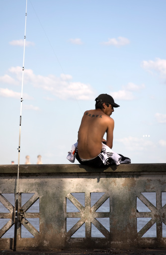 Buenos Aires, Argentina - October 15, 2011: A young man sitting on the edge of the pier, along with his fishing rod. Fisherman\'s Wharf in North Coast Avenue over RA-o de La Plata. Week end in Buenos Aires City.