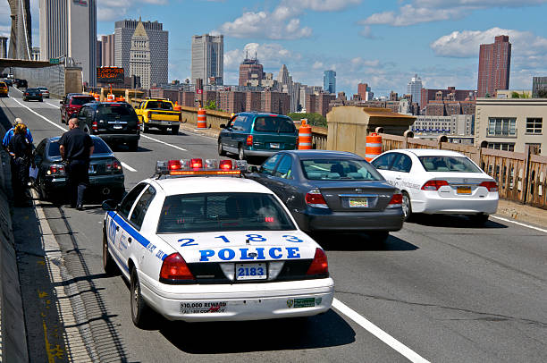 New York City, USA - August 22, 2011: A driver who\\'s automobile has a flat tire is seen being assisted by an NYPD officer on the Westbound roadway of the Brooklyn Bridge as other automobiles approach Manhattan in the distance.