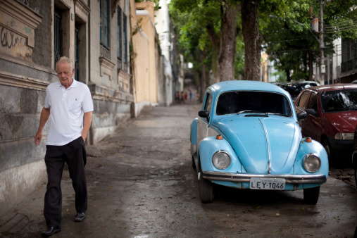 Rio de Janeiro, Brazil - March 5, 2011: An older gentleman walking down one of the old streets of Rio, past a Volkswago Bug parked on the sidewalk.