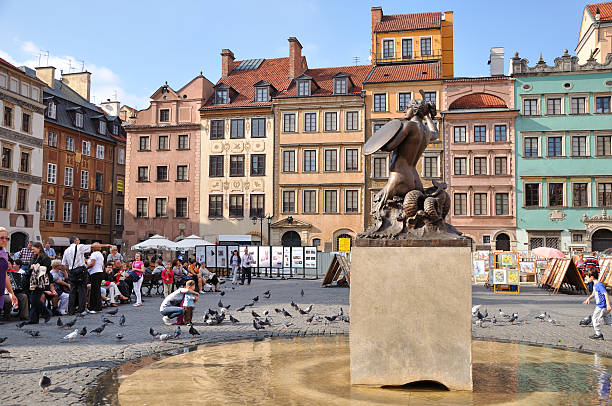 Warsaw, Poland - October 1st, 2011: Main Square of the Old Town. Warsaw Mermaid - symbol of the city - in front on the right side, many tourists looking visiting the place and feeding pigeons on the left side, and the colorful antique tenements in the background.