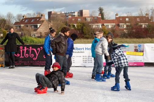 Maarssen, The Netherlands - December 12, 2011: Children having fun skating on the village Ice rink. A woman is watching.