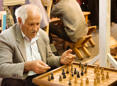 Sanliurfa, Turkey - May 21, 2011: An elderly man playing a board game named checkers with his friend in a tea house. Being very common in Middle East, tea house is a venue centered on drinking tea, playing games and spending time among men.
