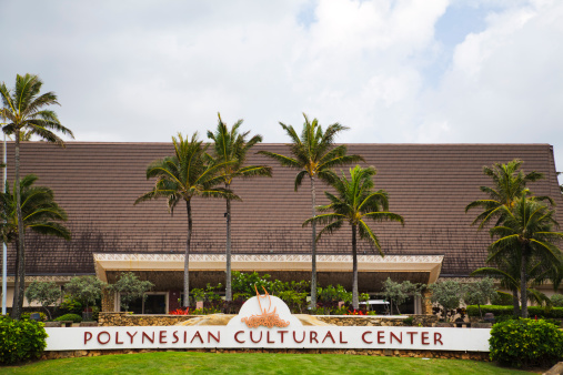 Laie, Hawaii, USA - June 2, 2011: The Polynesian Cultural Center (PCC) sign, palm trees, and building as seen from the attraction's main entrance. The PCC is located in northeast Oahu, and is one of the most visited sites in Hawaii.