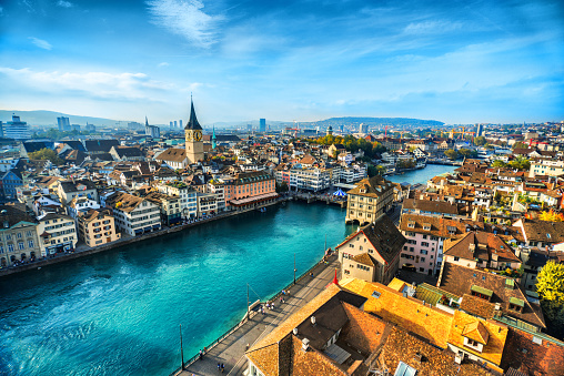 Aerial view of Zurich, Switzerland. Taken from a church tower overlooking the Limmat River. Beautiful blue sky with dramatic cloudscape over the city. Visible are many traditional Swiss houses, bridges and churches.