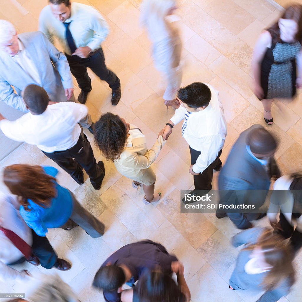 Business people shaking hands in busy crowded lobby Conference - Event Stock Photo