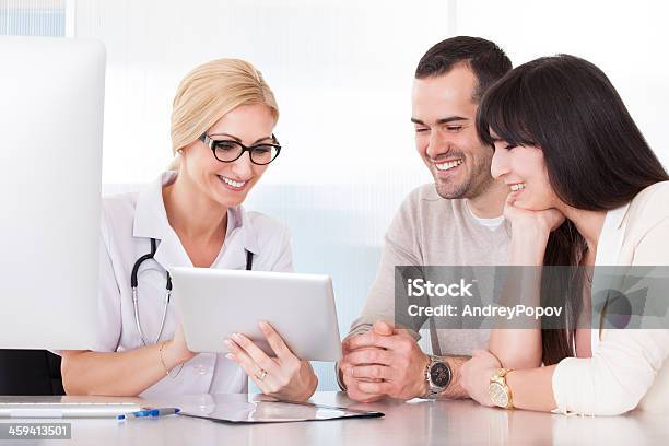 Medical Professional And Young Couple Smiling At Tablet Stock Photo - Download Image Now